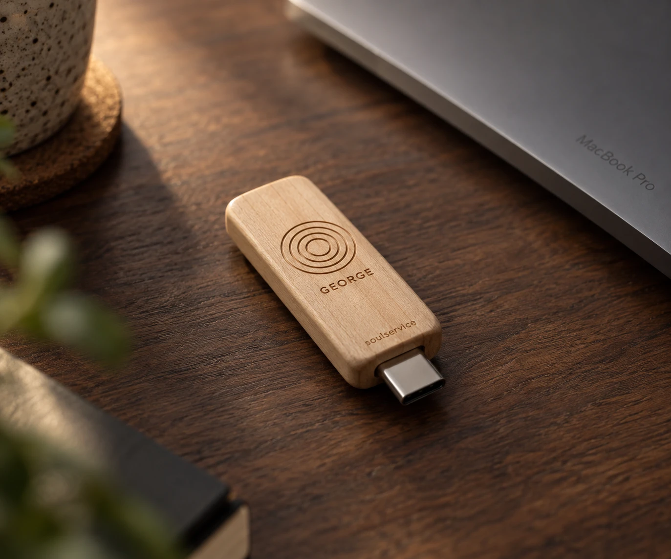 Soulservice Stick aus Holz mit eingraviertem Logo und dem Namen George, auf einem dunklen Schreibtisch neben einem MacBook